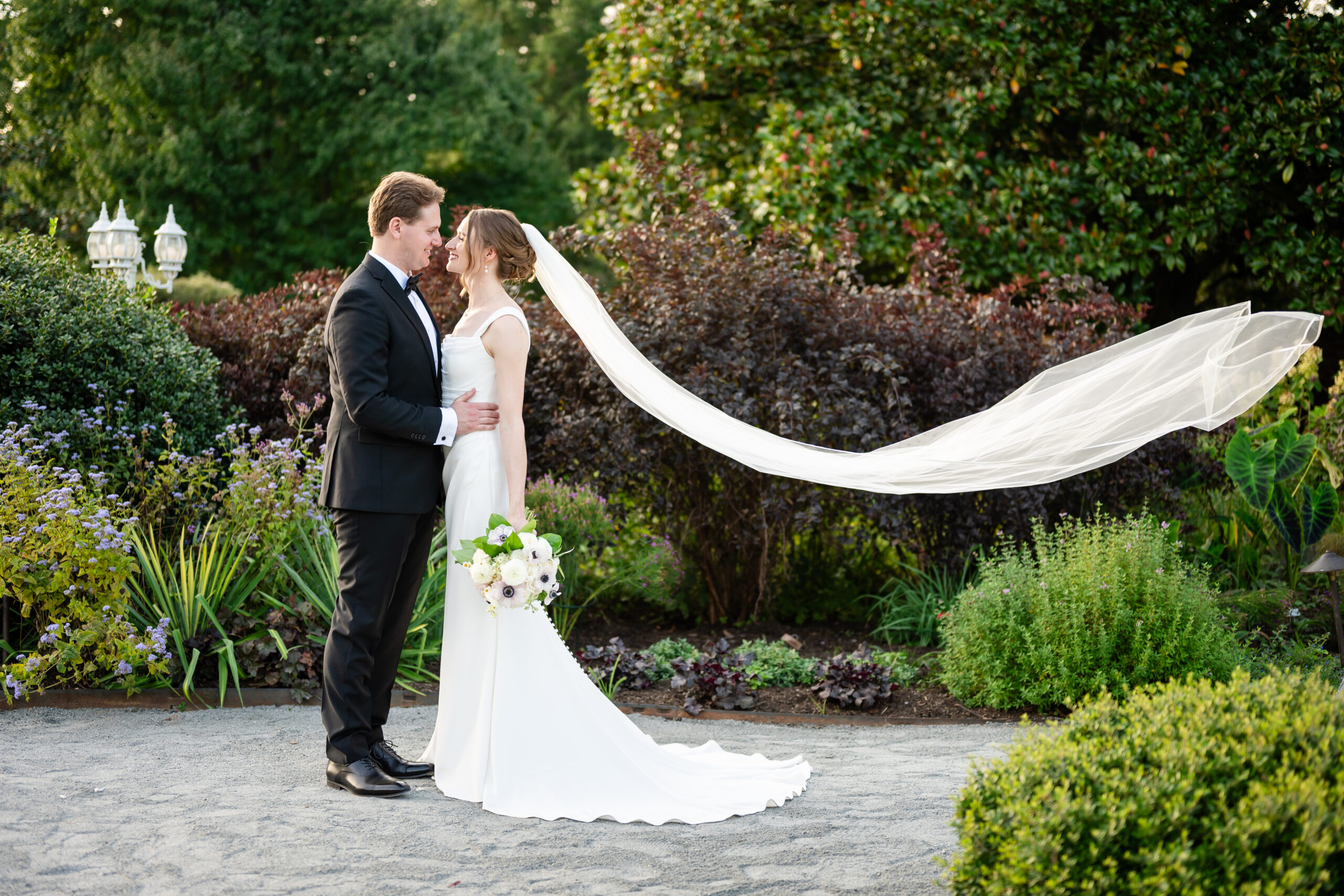 Bride And Groom Stand Facing Each Other In Garden At River Farm