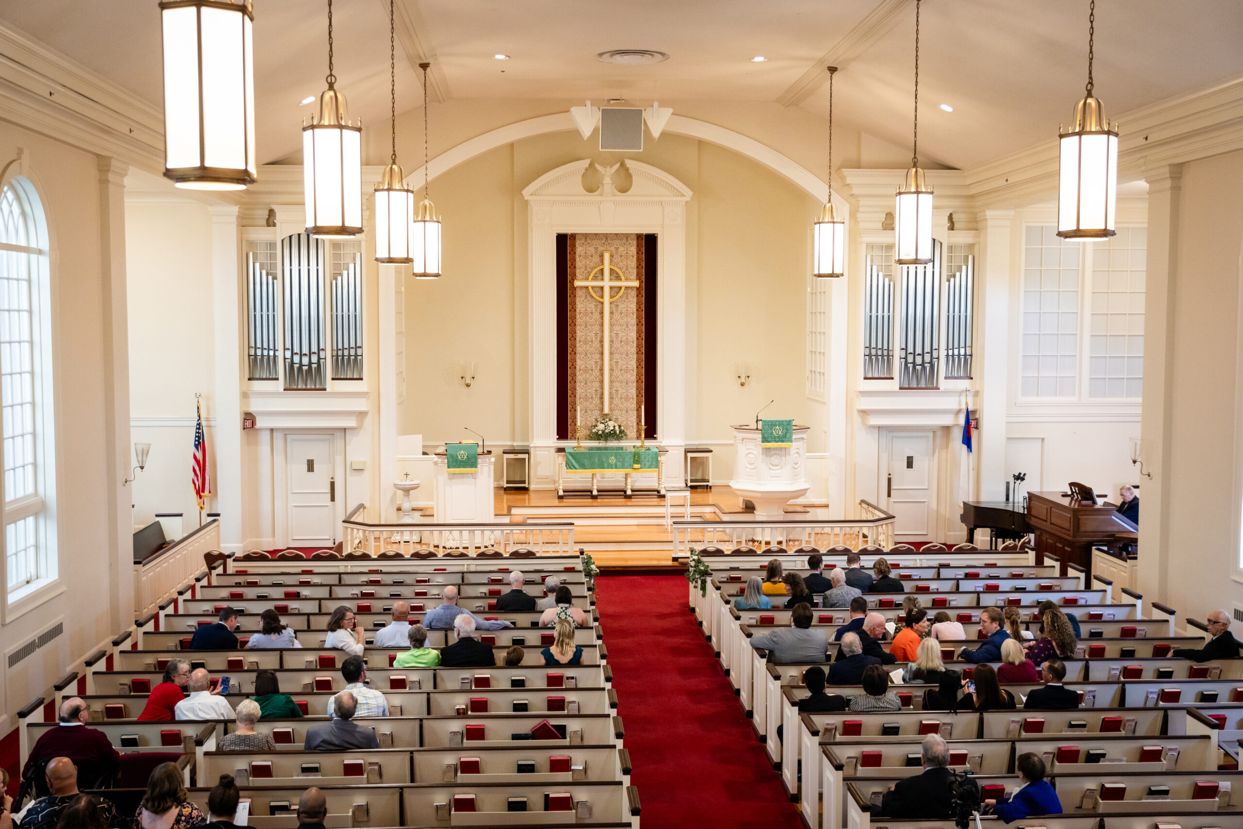 Congregation Sits In Pews Facing Altar Inside Bright Sanctuary Of Maine Of