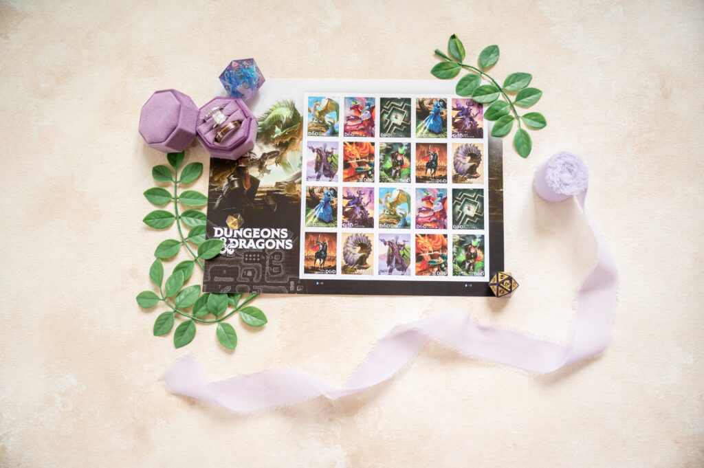 A sheet of Dungeons & Dragons-themed stamps is surrounded by green leaves, purple dice containers, polyhedral dice, and a light purple ribbon on a beige background.